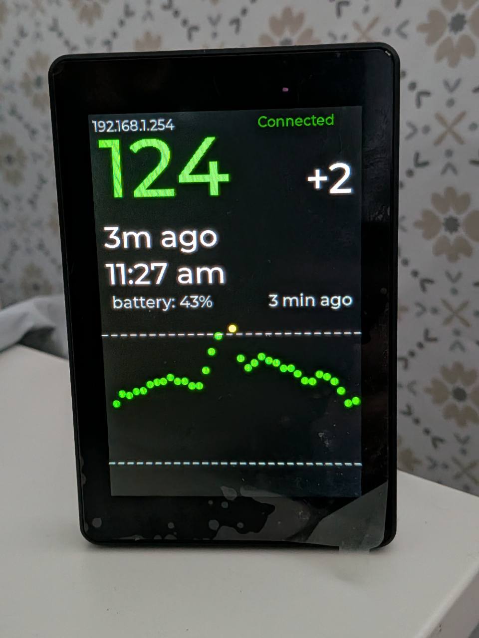 A black glucose display showing a large green reading and recent history