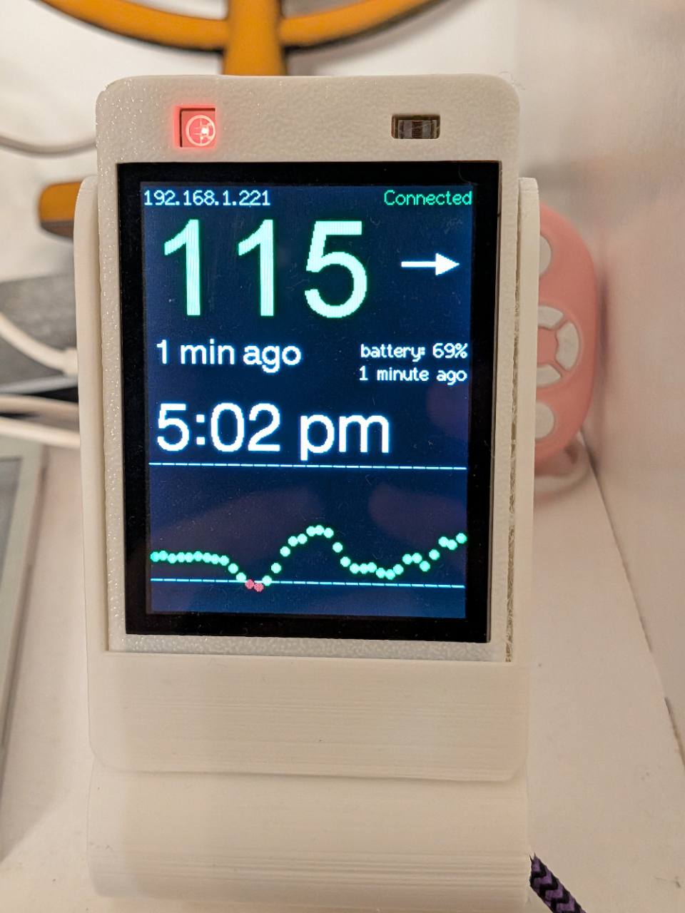 A white glucose display showing a trend arrow, reading age, and a history graph